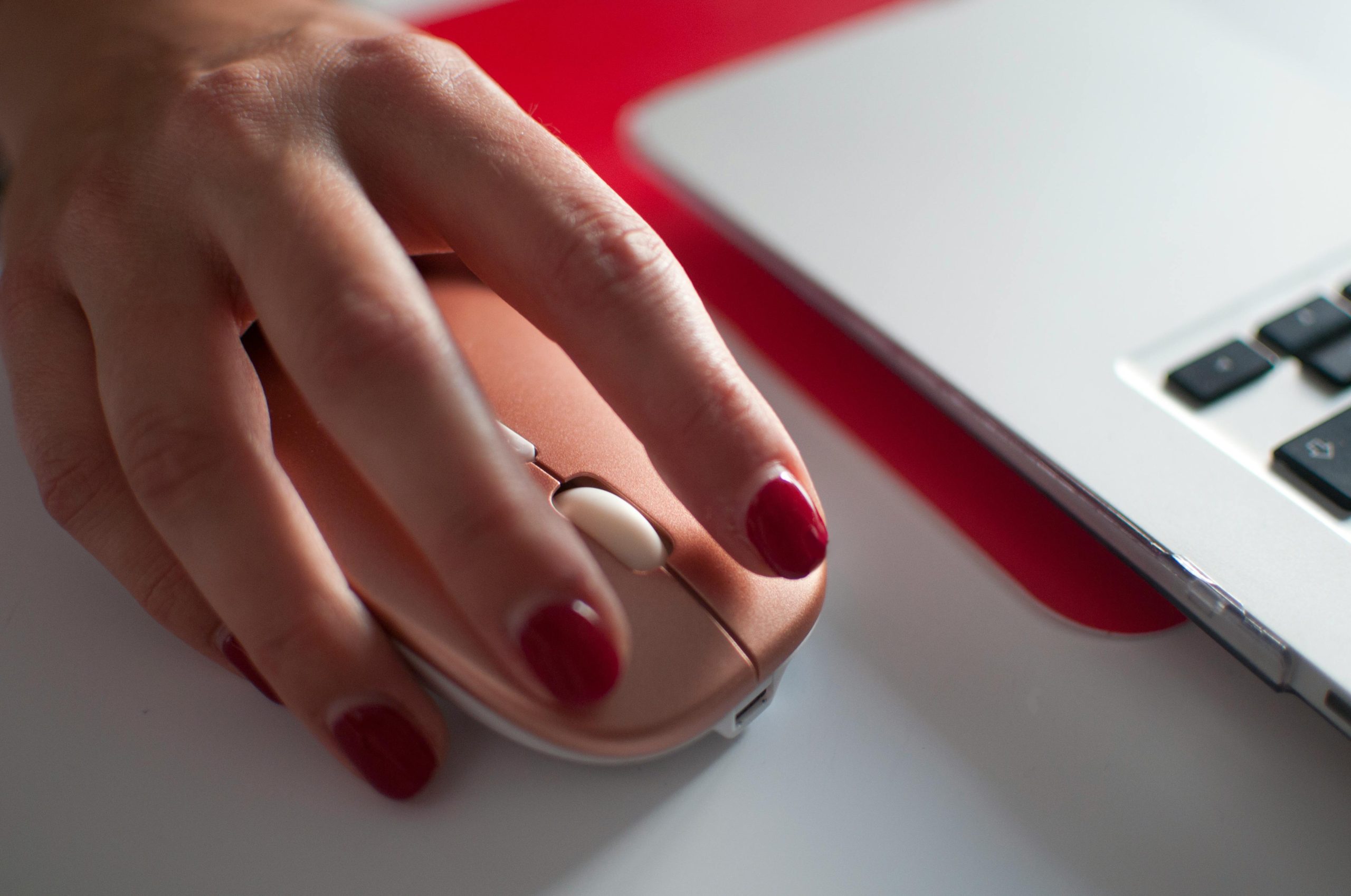 A womans hand with red nails clicking a pink computer mouse